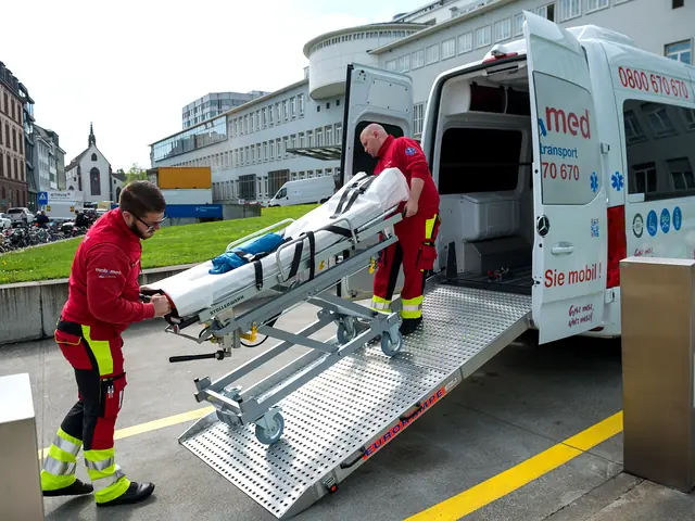 Zwei Mitarbeiter von Mobimed schieben eine Patiententrage über die Heckrampe in ein Transportfahrzeug