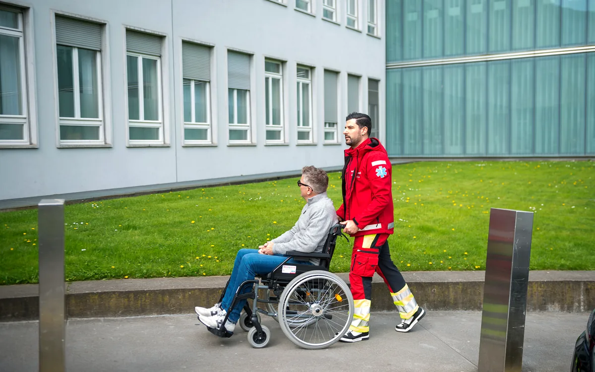 Mitarbeiter von Mobimed begleitet einen Patienten im Rollstuhl zum Behandlungstermin