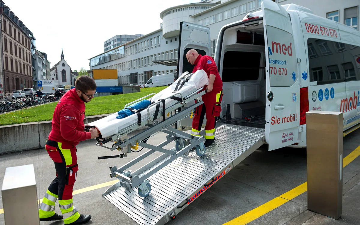 Zwei Mitarbeiter von Mobimed schieben eine Patiententrage über die Rampe ins Fahrzeug