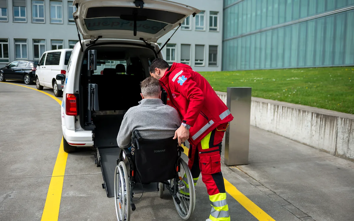Mitarbeiter von Mobimed schiebt einen Patienten im Rollstuhl über die Rampe ins Fahrzeug