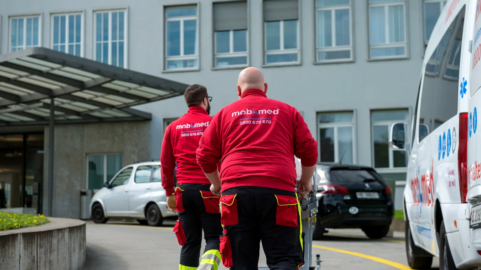 Zwei Mitarbeiter von Mobimed unterwegs mit der Trage vor einem Spital