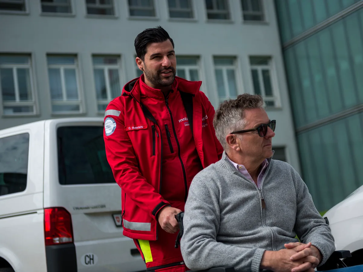 Mitarbeiter von Mobimed neben einem Patienten im Rollstuhl am Fahrzeug